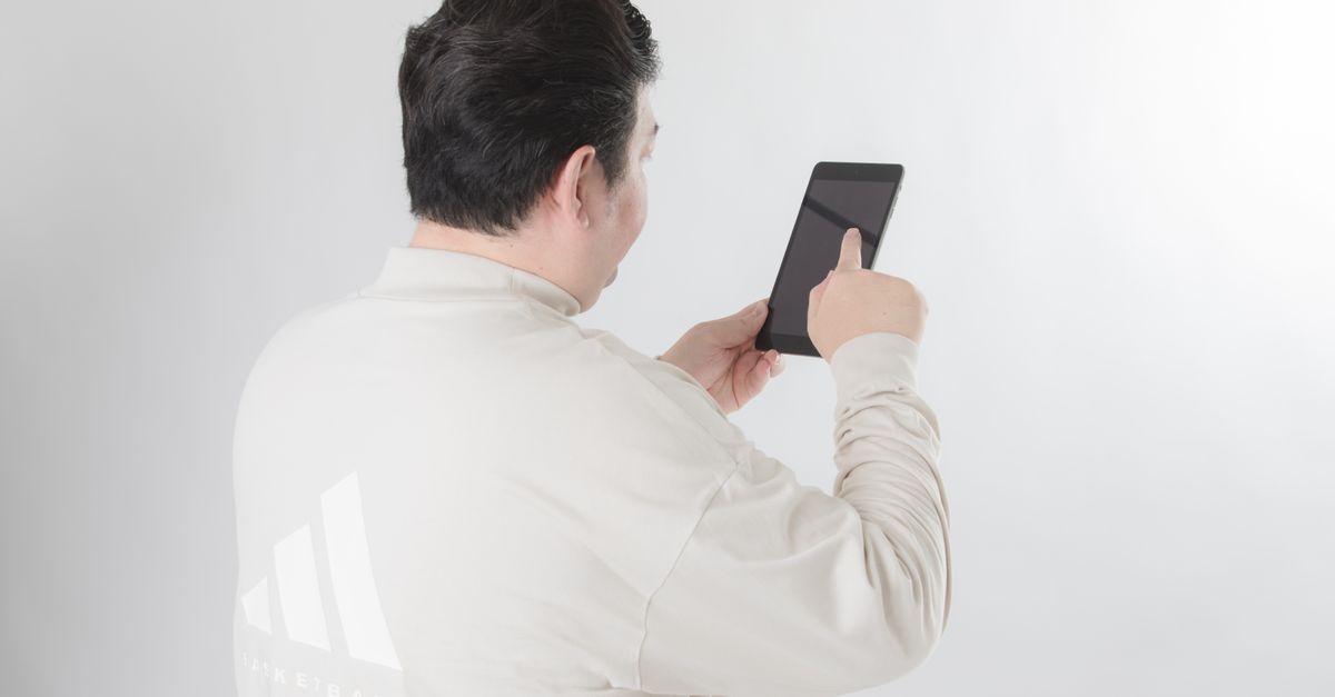 Man with black hair using a tablet on a white background, focusing on the screen.